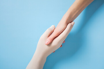 Two hands holding each other on a blue background, symbolizing support, connection, and unity between medical staff and patient