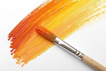 Fototapeta premium A paintbrush rests on a vibrant, freshly painted stroke of warm orange and yellow hues