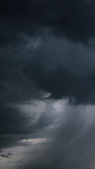 Fototapeta premium A dark, stormy sky with heavy clouds and streaks of rain indicates bad weather and an approaching windstorm, creating a dramatic and foreboding atmosphere.