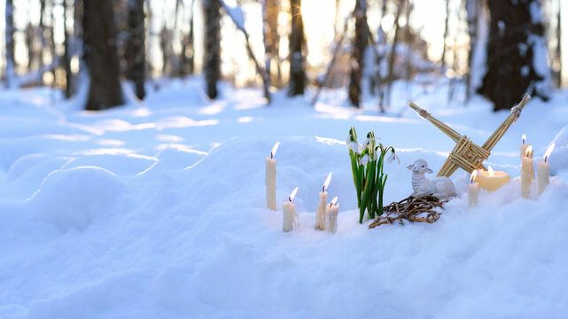 Wiccan altar for Imbolc holiday. witchcraft, pagan ritual. Brigid's cross, candles, snowdrops, toy sheep on snow, nature winter background. symbol of Imbolc, spring equinox.