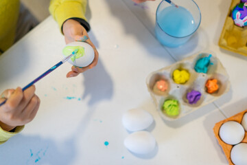 Child painting easter eggs on white table with paintbrush