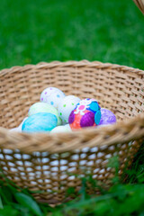 Wicker basket holding decorated easter eggs on green grass