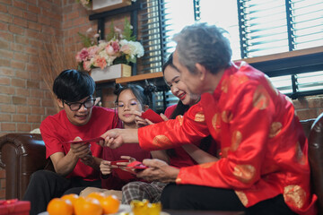 happy asian family gathering at home to celebrate Chinese New Year,sitting on couch,talking,giving red envelope and eating