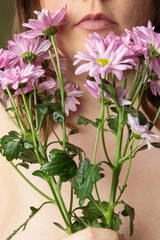 Curvy woman with clear skin imperfections in studio, purple daisy flowers and green background, unrecognizable