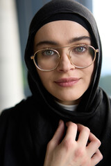 A stunning Muslim businesswoman is captured in a close-up portrait, showcasing her captivating green eyes behind stylish prescription glasses, radiating elegance and confidence