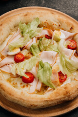 Gourmet salad pizza with lettuce, cherry tomatoes, turkey slices, and cheese on a wooden plate