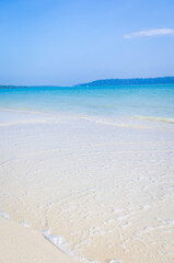 isolated pristine white sand beach with rolling waves and bright blue sky