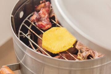 Smoker with cuts of meat and pineapple slice cooking in the smoke. Barbecue as a social gathering.