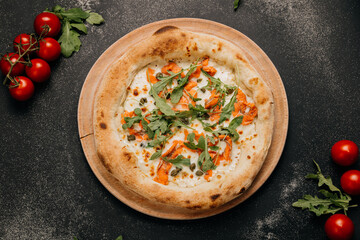 Gourmet pizza with smoked salmon, arugula, capers, and melted cheese on a wooden plate