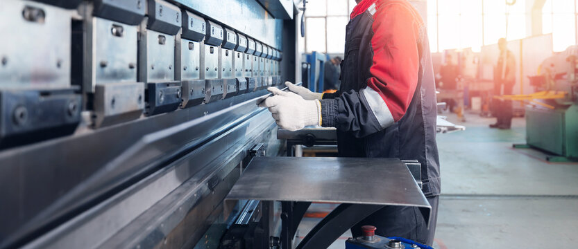 Caucasian male adult operating industrial press brake machine in factory setting