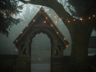 Lych gate at Church Entrance on winter foggy misty day covered in lights 