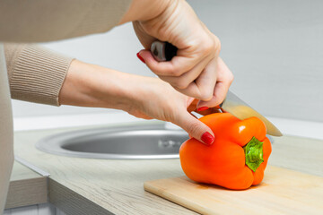 woman cutting red bell pepper with knife on kitchen board. knife cuts red bell pepper. 