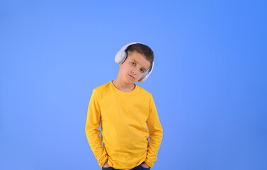 Portrait of cute serious boy listening music through headphones while standing on blue background