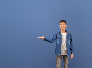 Portrait of young salesman smiling and showing empty palm while standing on isolated blue background