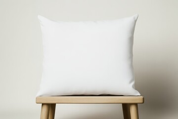 A simple white pillow rests on a wooden stool against a neutral background, creating a minimalist aesthetic.