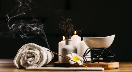 A set of cosmetics, burning candles, and a towel for spa treatments on a dark background, creating a serene atmosphere for relaxation and wellness.
