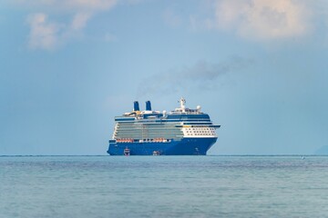 Large cruise ship sails peacefully on calm waters near a tropical coastline under a bright sky
