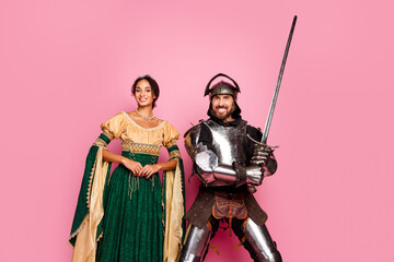 Naklejka premium Smiling Couple in Medieval Knight and Princess Costumes with Pink Background Depicting Romance and Ancient Era Inspiration