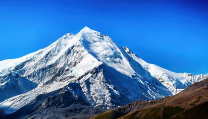 A snow-capped mountain peak rises majestically against a bright blue sky with brown hills visible in the foreground.