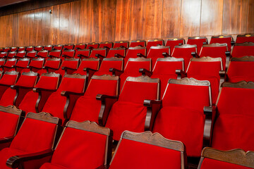 Obraz premium A close-up view of a theater's red-velvet seats with ornate wooden frames arranged in organized rows. The polished wood-paneled walls in the background enhance the warm, inviting atmosphere 
