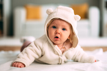 Baby girl wearing a soft comfortable bear-eared hooded jumpsuit, lying on her tummy on a blanket, exploring the world around her