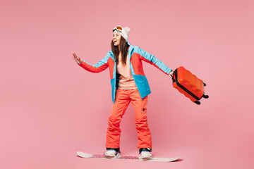 Traveler happy woman wears blue padded jacket ski goggles mask hold bag ride snowboard isolated on plain pink background. Tourist travel abroad in free time getaway. Air flight trip journey concept. © ViDi Studio