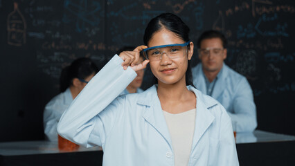 Highschool girl looking at camera while people doing experiment at laboratory. Young cute student...
