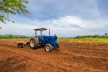 Obraz premium View of a blue industrial agricultural tractor preparing the soil with a plough and a automatic seed planter.