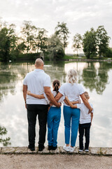 A family dressed in uniform white shirts stands together in a park by a pond