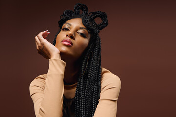 A young woman highlights her beauty with braids and a reflective pose in a warm setting.