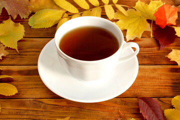 There is a cup of tea with autumn leaves on a wooden background
