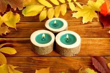 Three candles burn against a backdrop of autumn leaves.	