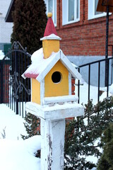 A beautiful wooden birdhouse stands under the snow in winter.