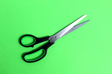 Black scissors lie on a green background with space for text.