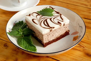 There is a plate with a fresh piece of sweet cake on the wooden table.