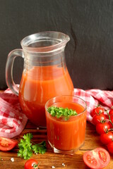 There is a jug and a glass of tomato juice on the wooden table.
