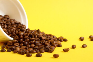 A white ceramic bowl with roasted coffee beans is overturned on a yellow background.