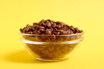 On a yellow background there is a transparent glass plate with roasted coffee beans.