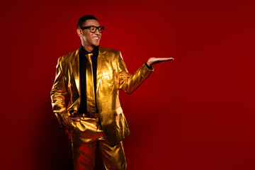 Elegant young man in glossy golden suit with a charismatic smile, posing confidently against a red...