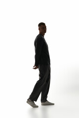 Young man walks elegantly wearing trendy attire, showcasing charisma in a modern setting.