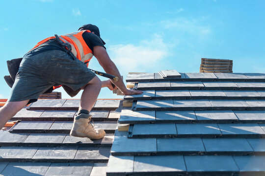 Roofer installing tiles on a bright day at a construction site with clear blue skies