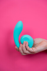 Hand with blue vibrator sticking out through pink paper background. Vertical photo. 