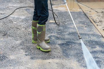 Worker cleaning asphalt surface with pressure jet washer at construction site