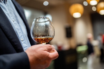 A person holding a glass of whiskey in a blurred, elegant indoor setting, creating a warm and sophisticated ambiance.