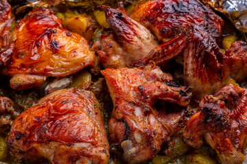 Crispy chicken pieces baked with potatoes in spices on foil close-up