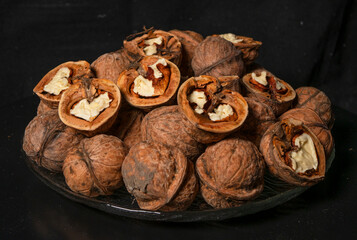 Peeled and whole walnuts lie on a glass plate. Black background.
