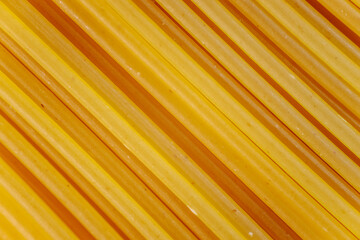 Close-up of neatly arranged uncooked dry spaghetti noodles in diagonal alignment. The golden-yellow texture highlights their smooth surface, ideal for food and cooking themes.