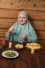 A woman in a light green hijab at a table with dates fingering her prayer beads reading dhikr