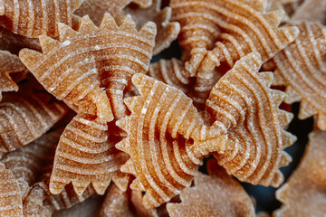 Close-up of dry bow-tie-shaped pasta with a ridged texture. The intricate patterns highlight its unique design, making it ideal for culinary-themed visuals and food concepts.