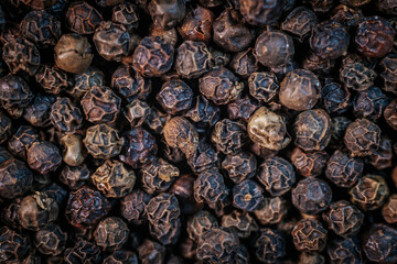 A close-up macro image of whole black peppercorns, showcasing their rich texture and dark brown tones. Perfect for culinary and spice-related themes.